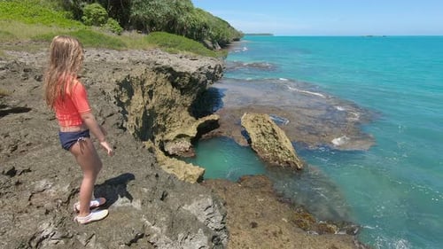 Young girl sprayed by mist from natural blowhole on rocky coast of Isle of Pines.