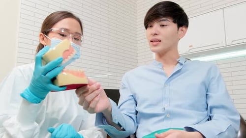 Asian female dentist explaining teeth care to a male patient in a dental clinic.