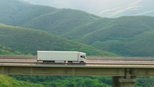 Cargo Delivery Truck Driving Along Scenic Mountain Viaduct Highway with Green Landscape