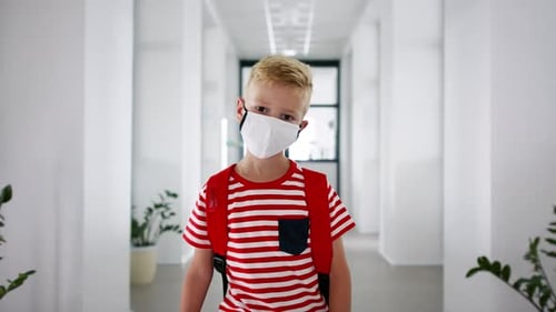 Small boy wearing face mask walking school corridor during coronavirus pandemic