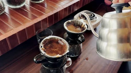 Die Hand des Barista gießt heißes Wasser aus einem Wasserkocher in Gläser mit Kaffee.