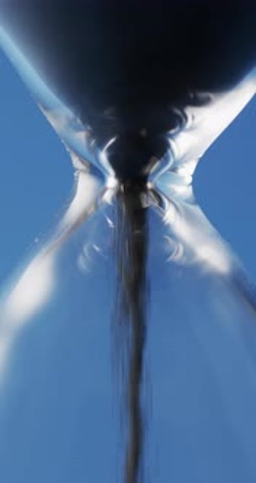 Vertical video of close up of hourglass with black sand pouring with copy space on blue background