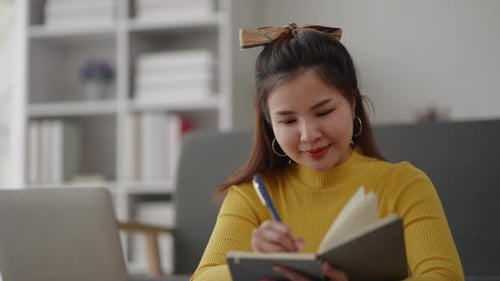 Woman Works at Home Using Laptop and Notebook