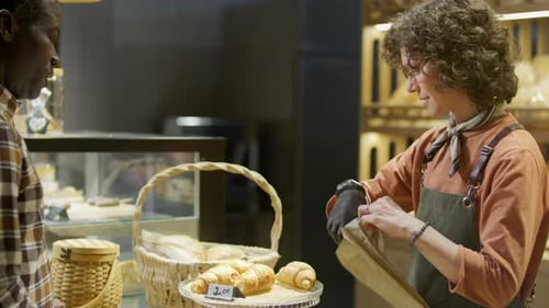 Friendly Female Baker Selling Fresh Croissants to Customer in Bakery