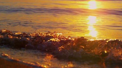 Nahaufnahme von Meereswellen, die beim goldenen Sonnenaufgang am Strand plätschern. Strahlende Sonne