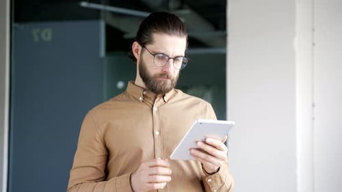 Portrait of smiling businessman using digital tablet standing at workplace in business office.