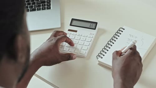 Man Calculating Numbers at Desk with Laptop