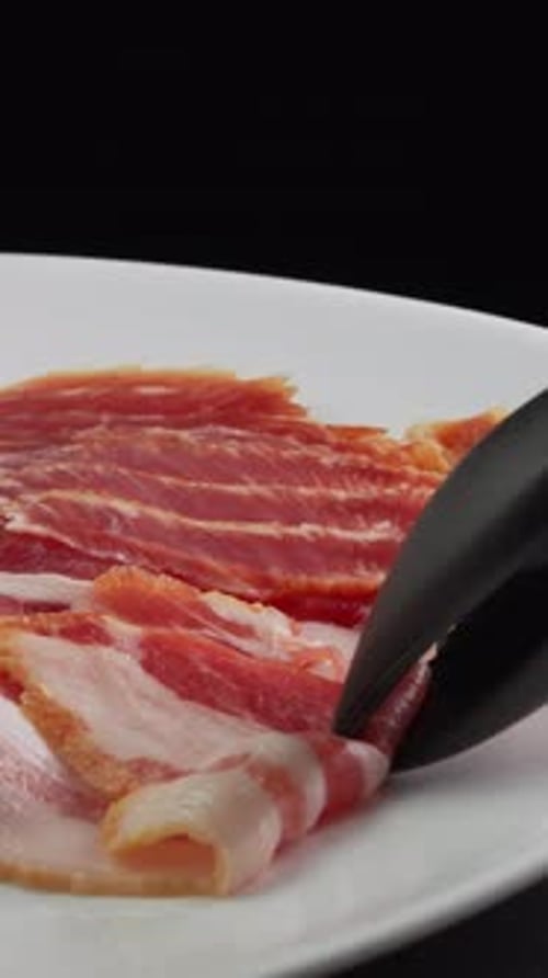 Vertical video Grill tongs take a strip of fresh bacon from the packaging. Pork meat with fat