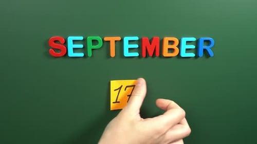 Hand sticking a sticker 17 September calendar day on school board. 17 date of September