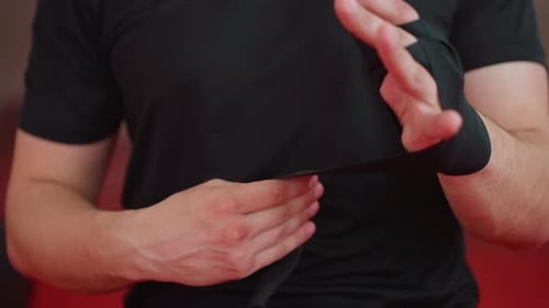 Boxer Wraps Fingers and Hands with Black Bandages Inside Gym