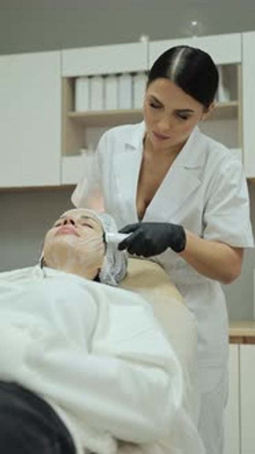 Woman Receiving Facial Treatment from Smiling Aesthetician Indoors