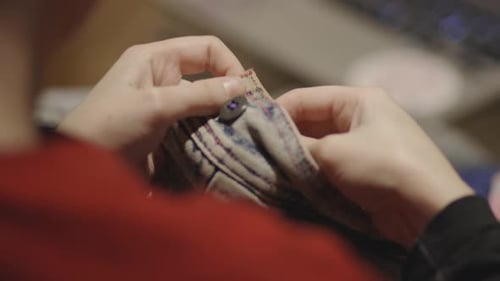 A Woman Sewing A Piece Of Button On A Faded Jeans. -close up shot