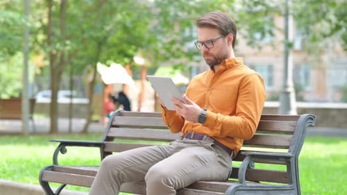 Young Adult Using Tablet on Bench in Park