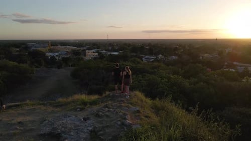 Wide angle drone shot of a couple standing together on top of a mountain while watching the sunset i