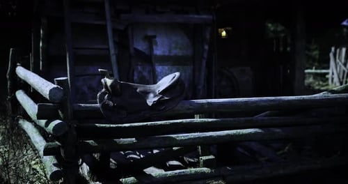 Saddle Resting on a Wooden Fence Near an Old Barn at Night