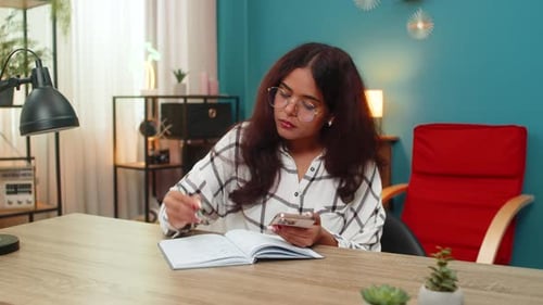 Une Indienne vérifie les informations de son smartphone avec référencement croisé, bloc-notes, étudiant des données, recherche en intérieur