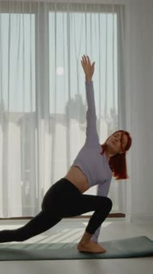 Vidéo verticale Une jeune rousse pratique le yoga dans un salon lumineux au lever du soleil