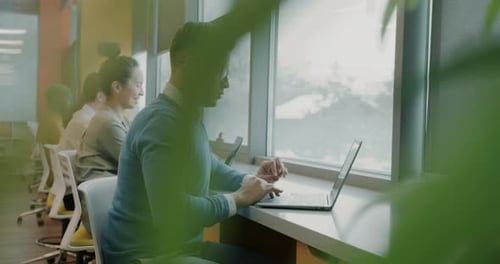 Multiethnic Group of Businesspeople Using Laptops Sitting at Desk in Modern Coworking Center