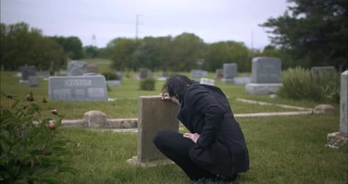Man mourning over death of loved one at grave tombstone in cemetery.