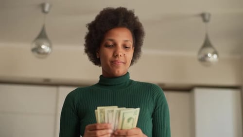 Lowangle View Portrait of Serious AfricanAmerican Young Woman Holding Counting Dollar Banknotes at