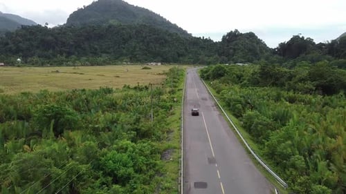 Aerial view of a car riding on the highway through the forest on the countryside.