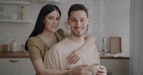 Smiling Couple Embraces in Kitchen with Coffee
