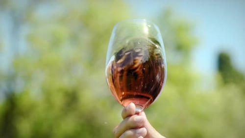 Hand stirs rose wine in glass outdoors