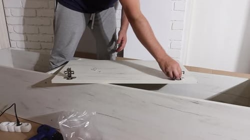 Young Adult Attaches Hinges to Furniture Panel