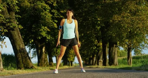 a happy girl fit relaxed jogging and running in a street with trees and nature, using headphones f