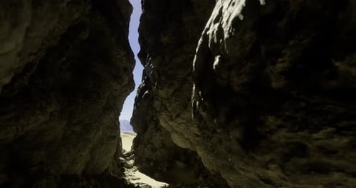 Narrow Rock Crevice Leading to Bright Desert Landscape Under Clear Sky