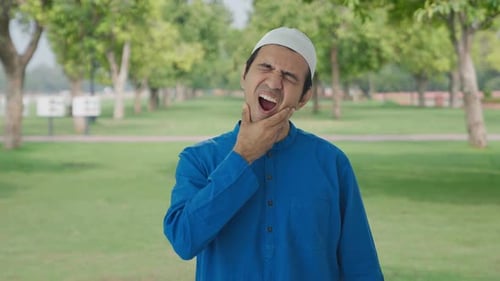 Sick Muslim man suffering from tooth pain in park