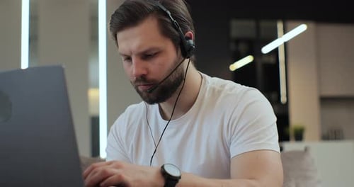 Focused Young Adult Works on Laptop With Headset