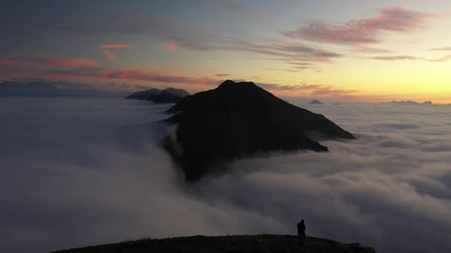A man walks by himself on the edge of a mountain at extreme altitude with a sea of clouds in front o