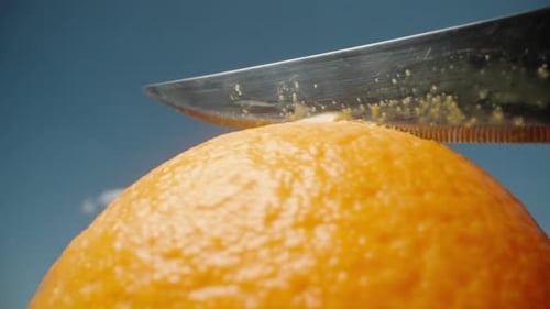 Je découpe une orange avec un couteau sur le ciel bleu. macro, Ralenti.