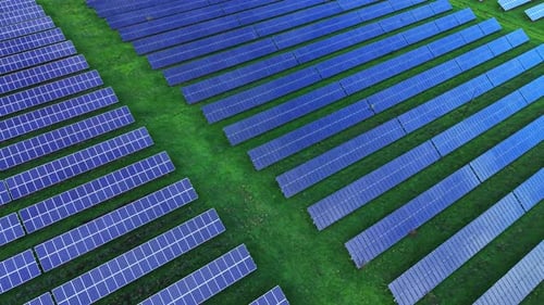 Solar panels arranged in neat rows on green field under clear sky