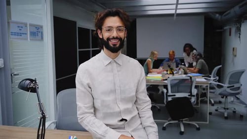 Video of Happy Young Leader Sitting and Looking Camera While Colleagues Work in Background