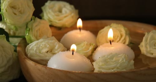 Floating candles and white roses in wooden bowl