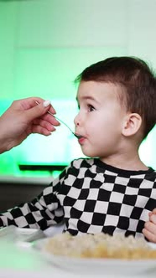 Garotinho jantando com a mãe. Nutrição para bebês famintos. Vídeo vertical
