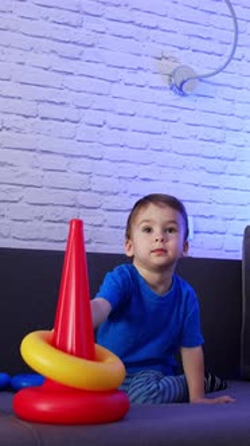 Lindo niño de pelo oscuro montando una pirámide en el sofá. El bebé juega con un juguete en casa.