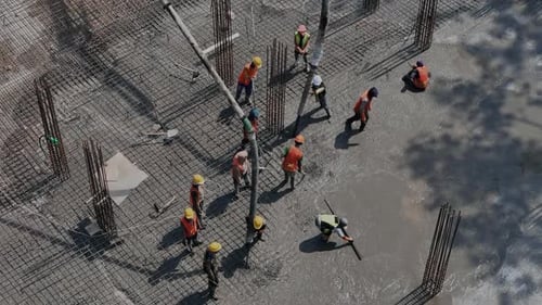 Vista aérea de trabajadores vertiendo y nivelando cimientos de concreto