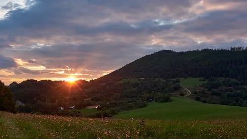 Epischer Sonnenuntergang über den Hügeln auf einer grünen Wiese auf dem Land im Sommer
