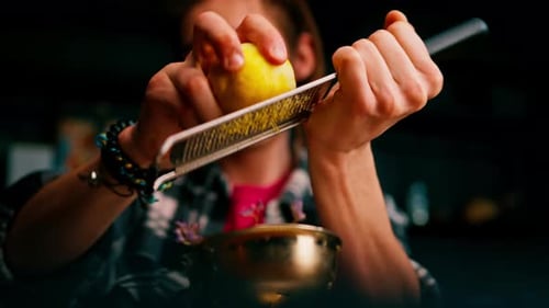 Männliche Hände eines Barkeepers reiben die Schale einer Orangenfrucht für einen Cocktail mit einer speziellen Reibe ab