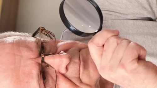 Senior Man Examining Face with Magnifying Glass Close-up