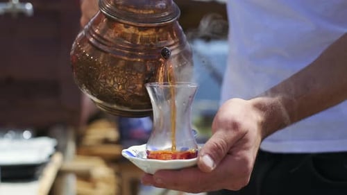 Traditioneller türkischer Tee, der in ein traditionelles türkisches Teeglas gegossen wird. Zeitlupe in 4K.