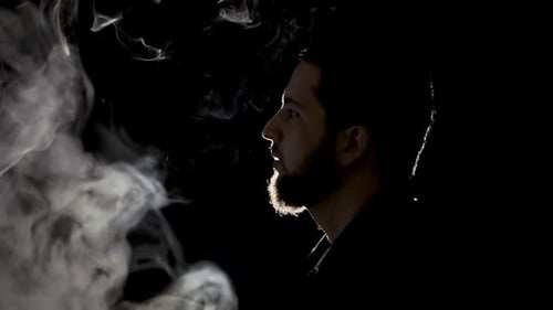Bearded man blowing smoke in dark background