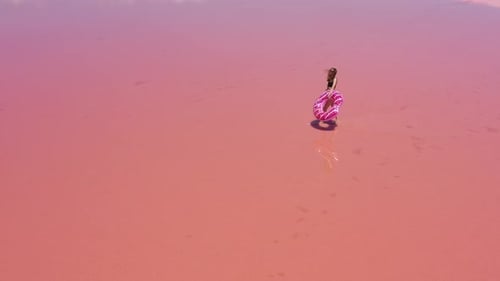 Vista aérea. Jovem mulher de maiô preto carrega uma bóia rosa inflável nas mãos, divirta-se