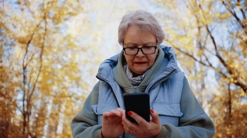 Senior Woman Using Phone in Autumn Park