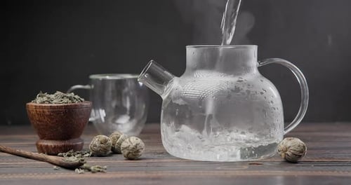 Pouring Water into Glass Teapot with Green Tea