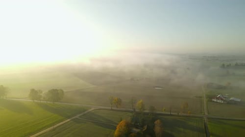 Beautiful aerial view of fog rolling over rural countryside farmland at sunrise