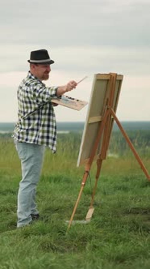 Artist in Hat and Checkered Shirt Painting in a Peaceful Grass Field